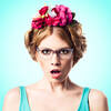 Portrait einer Frau mit Brille und großem Haarschmuck aus roten Blumen mit empörtem Gesichtsausdruck.