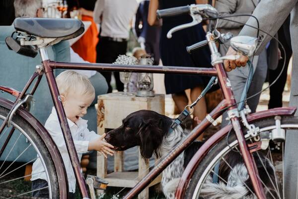Blick durch das Gestänge eines alten Rades auf ein Kind, das voller Freude einen Hund an der Schnauze streichelt.