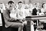 Ein Brautpaar in der Kirche sitzend, zwei Kinder am Schoß, eines hat einen Lolly, das andere schaut mit geöffnetem Mund auf den Lolly. Schwarz-Weiß.