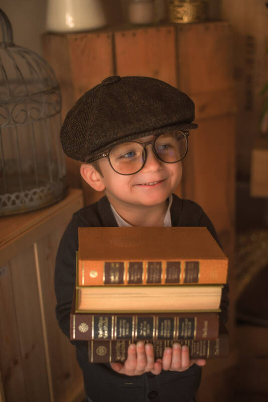 Ein Bub mit Schirmmütze und großer Brille hält einen Stapel alter Bücher in den Händen