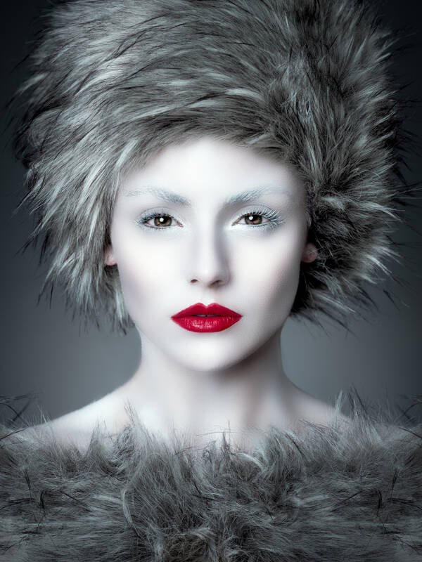 Portrait einer blass geschminkten Frau mit intensiv rotgeschminkten Lippen. Kopfbedeckung und Kleidung aus weiß-grauem Pelz.