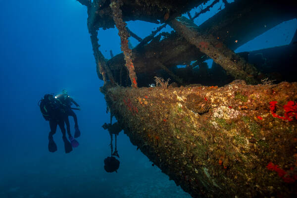 Unterwasseraufnahme zweier Taucher neben einem gesunkenen Schiff.