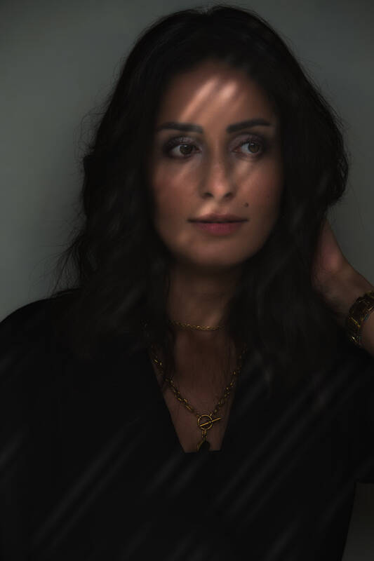 Portrait einer Frau, die durch schräg von rechts oben einfallende Lichtstreifen beleuchtet wird. 