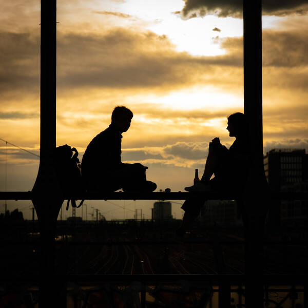 Silhouette zweier junger Menschen, die auf einm Gerüst sitzen gegen einen abendlichen Himmel.