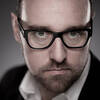 Close-up Portrait eines bärtigen Mannes mit schwarz gerahmter Brille.