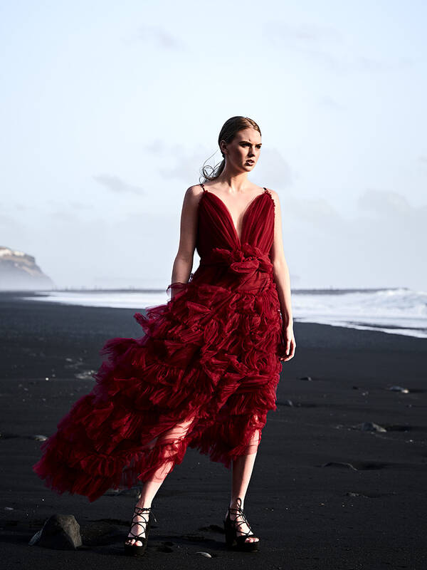 Model mit rotem Kleid auf einem Lavastrand.