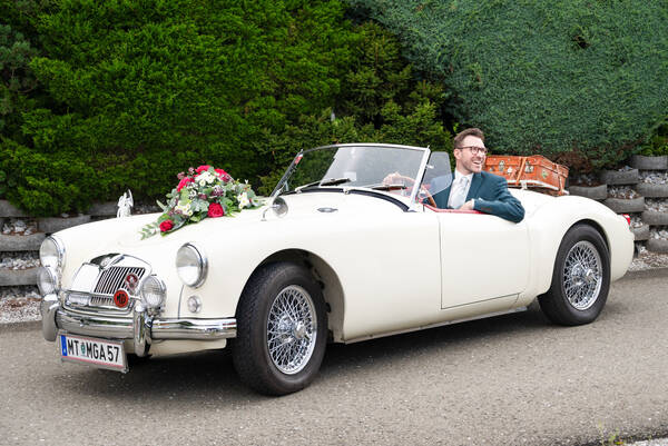 Bräutigam in einnem Oldtimer Cabriolet mit Blumenschmuck.