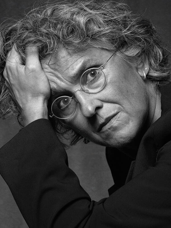 Portrait einer Frau mit runder Brille, die ihren Kopf in die Hand stützt. Schwarz-Weiß