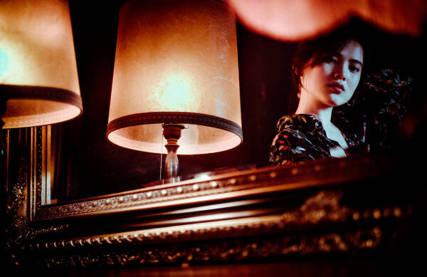 Portrait einer jungen Frau neben einer Leuchte in einem Spiegel mit antikem Rahmen.