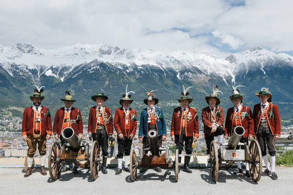 Gruppenbild einer Tiroler Schützenkompanie mit drei Mörserkanonen am Bergisel mit Blick über Innsbruck und die oberhalb der Seegrube verschneite Nordkette.ö
