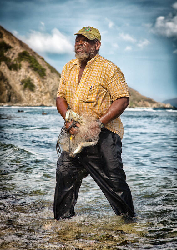 Ein dunkelhäutiger Mann in buntem Hemd steht im Wasser am Strand und hat ein Netz mit einigen kleinen Fischen in der Hand