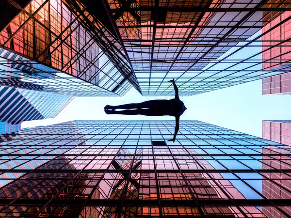 Ein Mensch schwebt mit ausgestreckten Armen zwischen spiegelverglasten Hochhäusern.