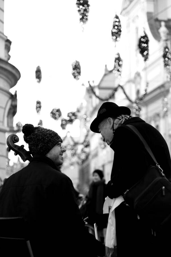 Eine ältere Dame steht bei einem Straßenmusikanten mit einem Cello in der Vorweihnachtszeit. Schwarz-Weiß.