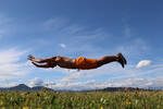 Ein Mann mit nacktem Oberkörper schwebt im Sprung über einer Blumenwiese.