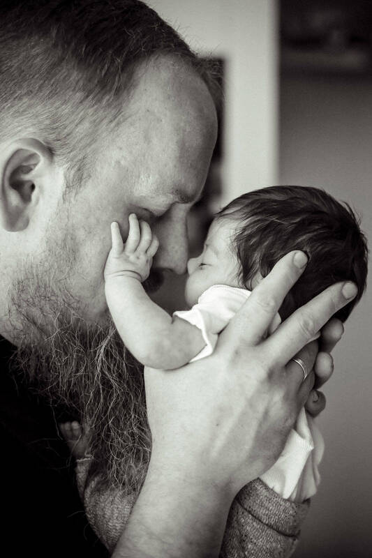 Ein bärtiger Mann hält ein neugeborenes Baby so vor sein Gesicht, dass sich die Nasenspitzen berühren. Beide haben die Augen geschlossen. Schwarz-Weiß.