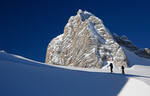 Winterlandschaft  am Dachstein mit dunkelblauem Himmel. Zwei Schitourengeher gehen von rechts nach links durch das Bild. ihre schattige Silhouette hebt sich deutlich vom hellen Schnee ab.