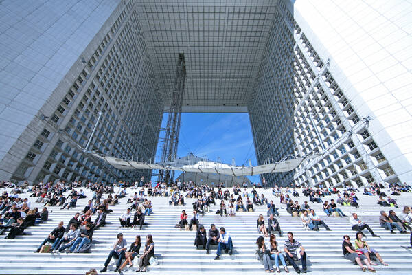 Menschen sitzen auf der Stiege des Grand Arche in Paris.