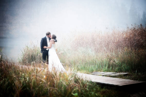 Ein Brautpaar auf einem Steg an einem See im Nebel.