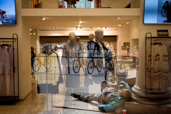 Blick durch ein Schaufenster in ein Bekleidungsgeschäft. durch die Spiegelung in der Scheibe wirkt es so, als ob ein Mann, der außerhalb des Geschäftes auf dem Gehsteig liegt, im Geschäft liegen würde.,