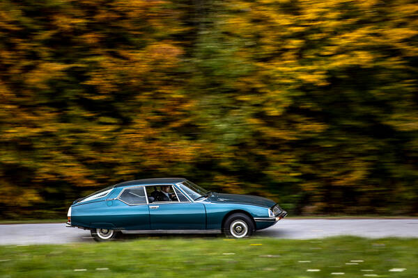 Ein Mann fährt in einem petrolfarbenen Citroen SM durch herbstliche Landschaft. Bewegungsunschärfe.
