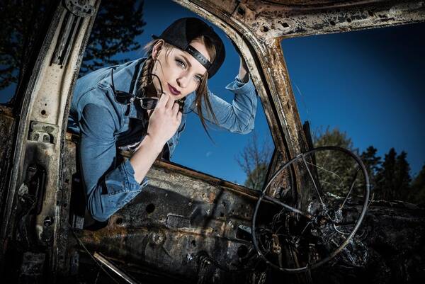 Eine junge Frau mit Baseball-Kappe lehnt sich von außen in ein altes abgewracktes Auto.