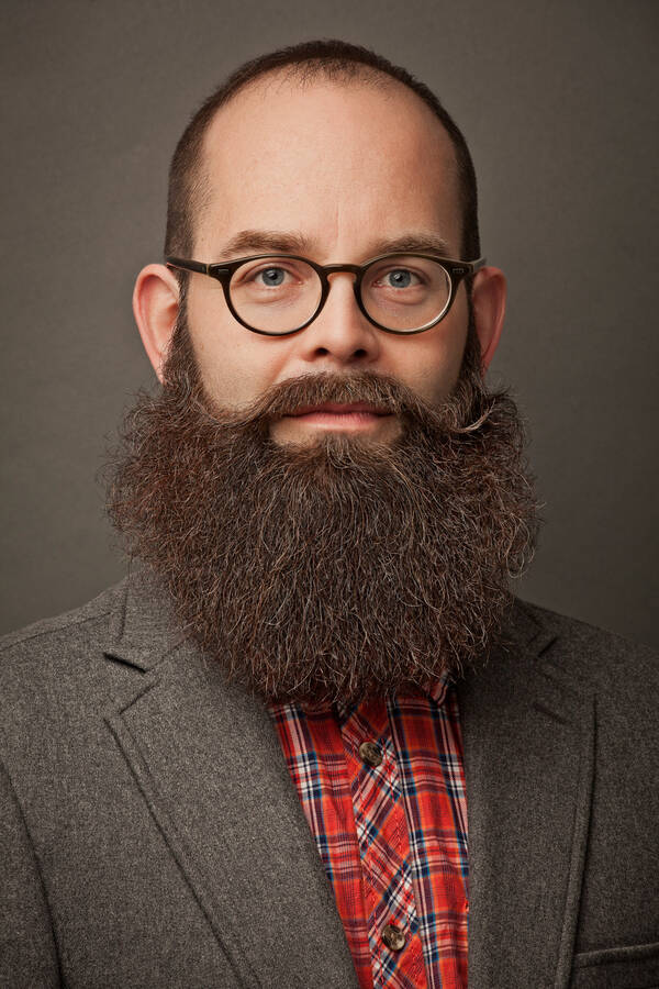 Portrait eines Mannes mit kurzen Haaren, hoher Stirn, Brille und sehr gepflegtem, üppigem Bart.