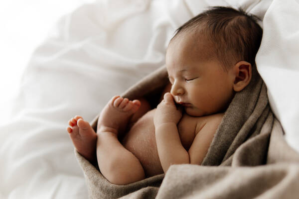 Ein Baby schläft eingewickelt in ein braunes Tuch auf weißem Untergrund.