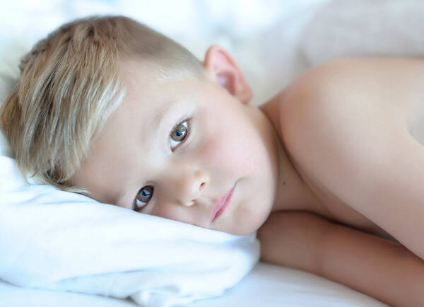 Portrait eines blonden Buben, der im Bett liegt.