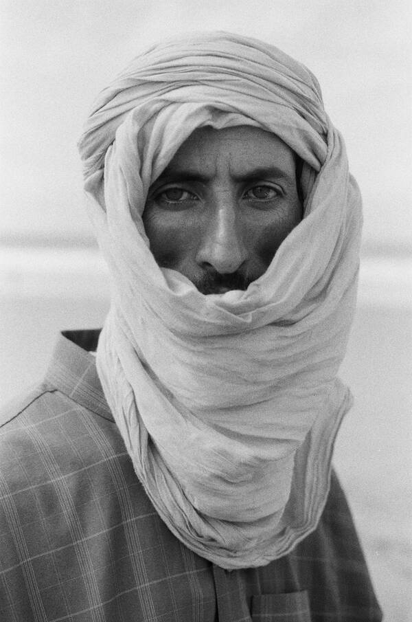 Ein Mann in einer Wüste trägt ein Tuch um seinen Kopf und das Gesicht geschlungen. Schwarz-Weiß.