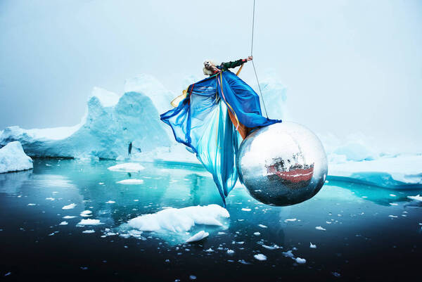 Eine Person in glamourösen Roben schwingt auf einer Diskokugel über Packeis.