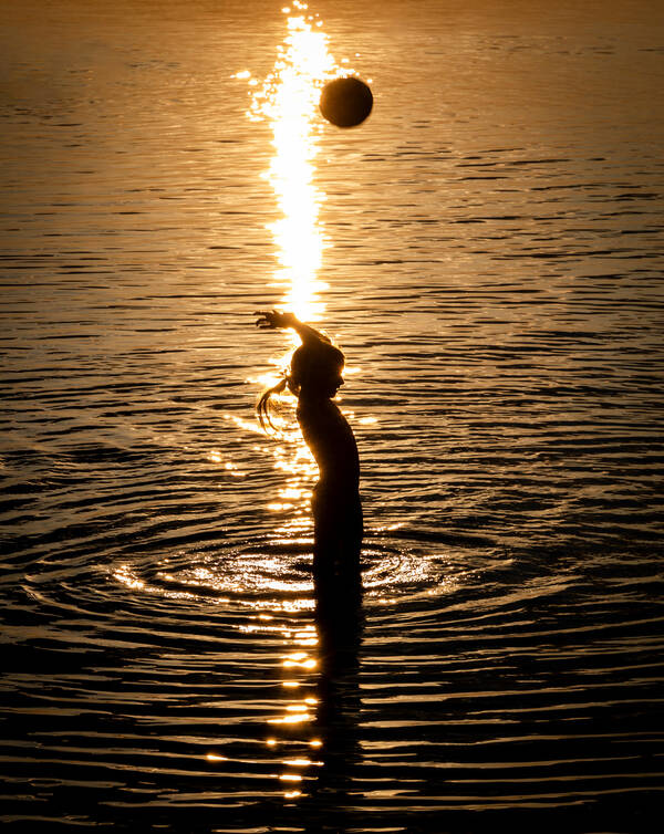 Ein Mädchen spielt in der Abendsonne mit einem Ball im Wasser.