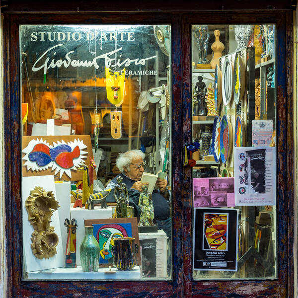 Blick durch das Schaufenster in das Keramik-Atelier von Giovanni Fisco. Inmitten vieler Keramikarbeiten sitzt der Künstlier und liest.