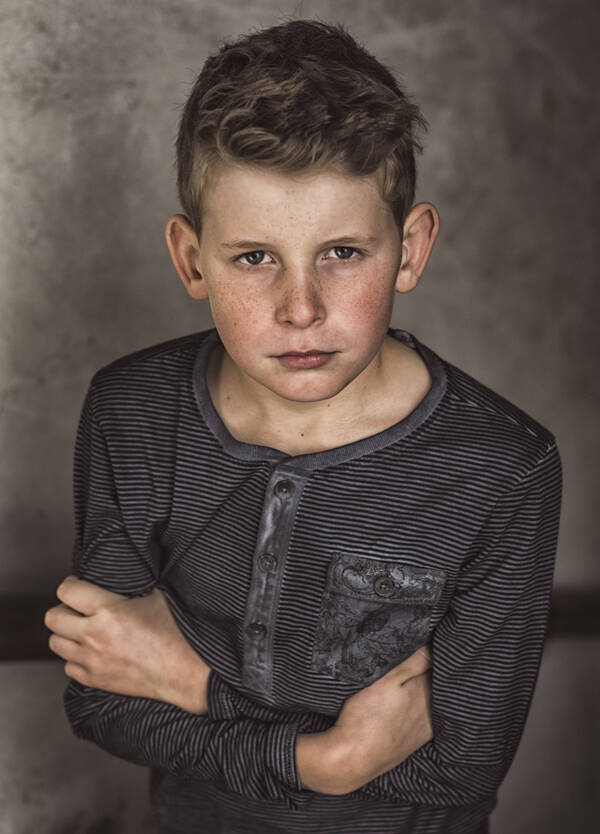 Portrai eines Buben mit Sommersprossen in dunkel gestreiftem Shirt, Arme verschränkt