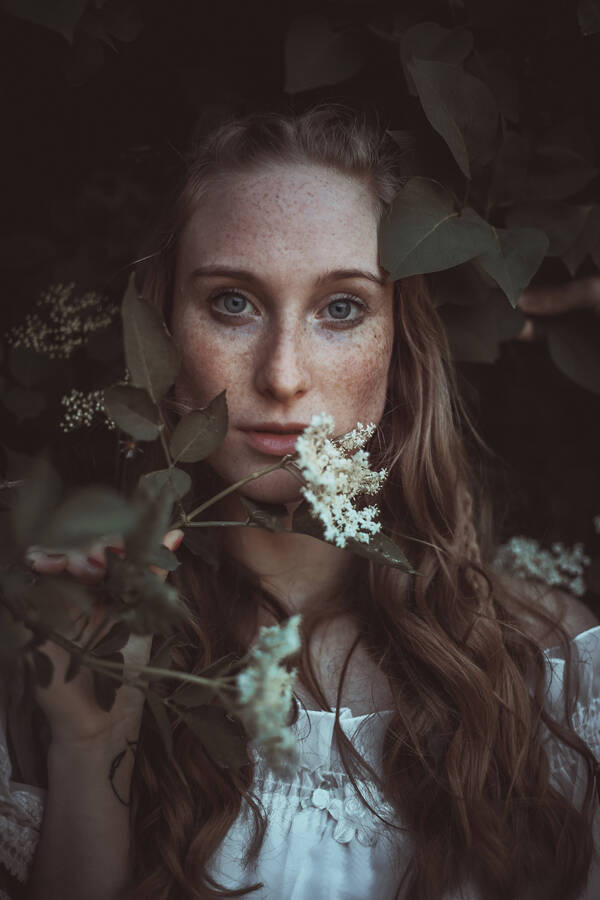 Portrait einer Frau mit langen Haaren, im Vordergrund Hollerblüten.
