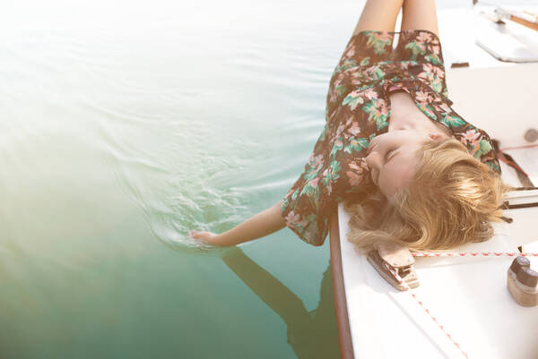 Eine junge Frau liegt an Deck eines Bootes und lässt die Hand ins Wasser gleiten.