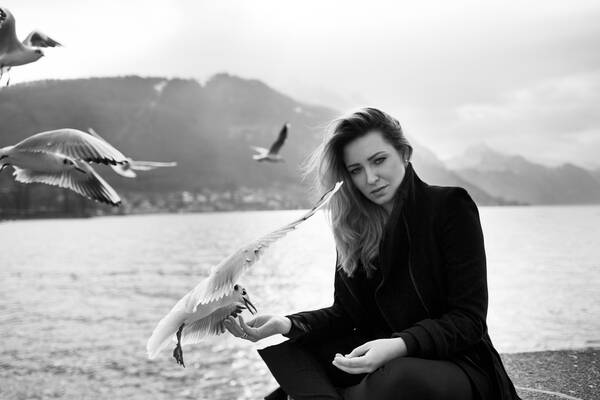Eine Frau sitzt an einem See und füttert Möwen. Schwarz-Weiß.