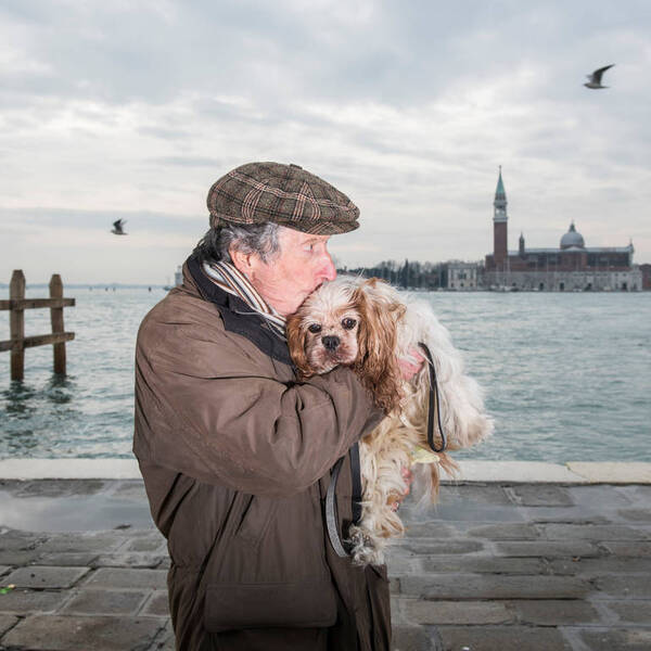 Ein älterer Mann trägt einen Schoßhund in Venedig.