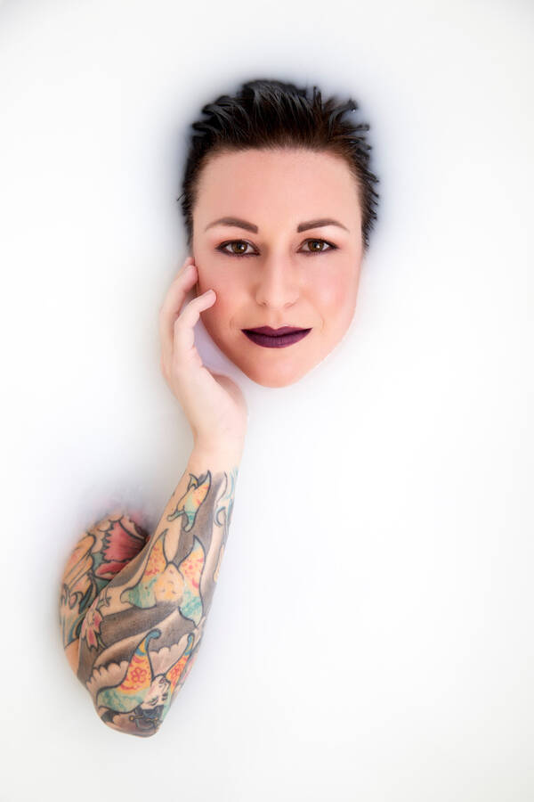 Eine Frau liegt in einer milchigen Flüssigkeit. Nur das Gesicht und ein stark tätowierter Arm sind sichtbar.