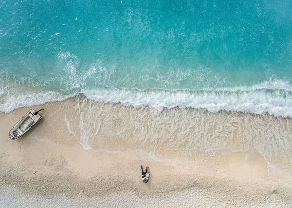 Drohnenaufnahme eines Brautpaares, das eng umschlungen auf einem Sandstrand liegt. 