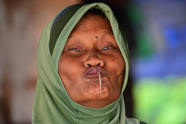 eine mit grünem Kopftuch verhüllte Frau saugt eine Nudel ein.