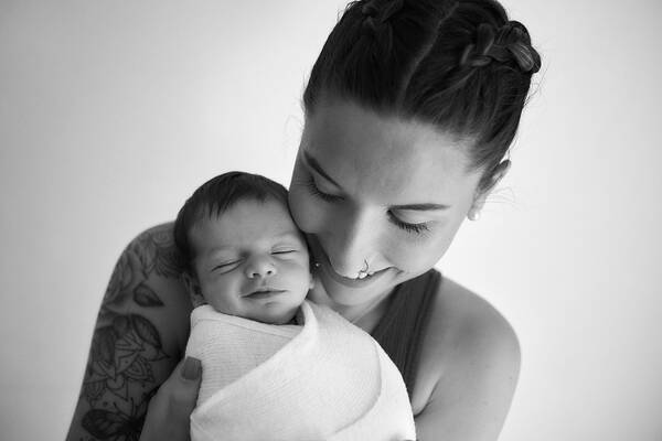Portrait einer tätowierten Frau, die ein eingewickeltes Baby hält. Schwarz-Weiß.