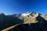 Eine Gruppe von Bergsteigern ist winzig klein auf einem Berggrat zu erkennen. Im Hintergrund das Glocknermassiv unter strahlend blauem Himmel.