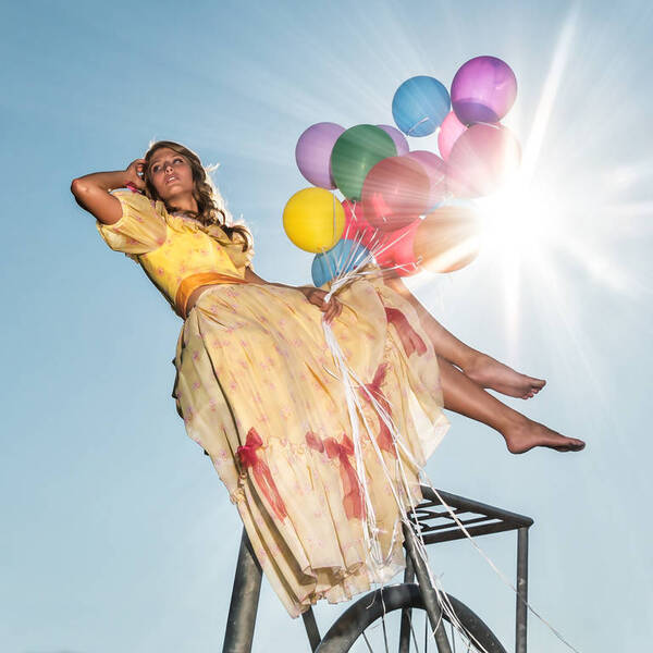 Frau mit bunten Luftballons sitzt auf einem überdimensionalen Fahrrad