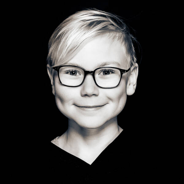 Portrait eines blonden Kindes mit dunkler Brille. Schwarz-Weiß.