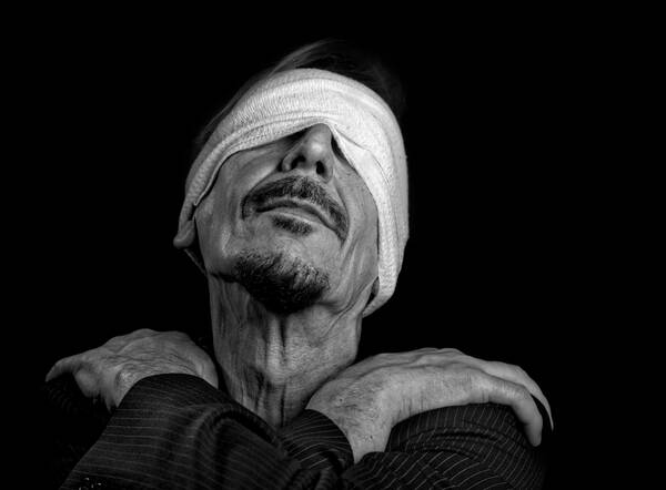 Ein Mann mit Verbundenen Augen, die Hände über Kreuz auf den eigenen Schultern. Schwarz-Weiß