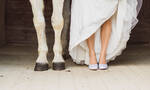 Detailaufnahme von den Beinen eines weißen Pferdes und einer Braut, die ihr Kleid hebt, so dass man ihre Beine sehen kann.