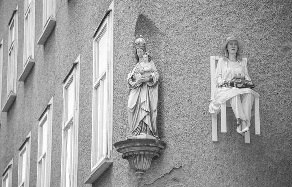 Fassade eine Hauses mit einer Marienstatue, an der Hauswand ist ein Sessel befestigt, auf dem eine Frau in weißen Gewändern sitzt. Schwarz-Weiß.