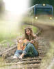 Junge Frau mit Blumenkranz sitzt Gitarre spielend auf den Geleisen, im Hintergrund kommt ein Zug.