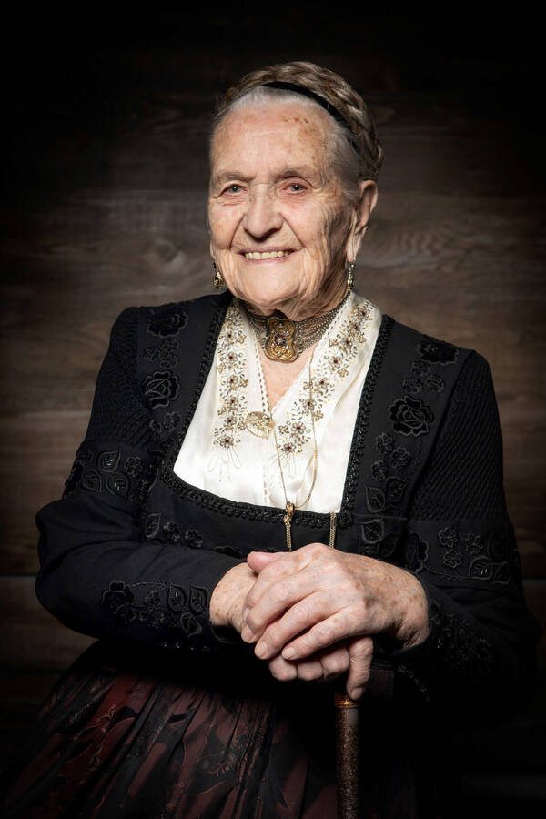 Portrait einer alten Frau in eleganter, reichbestickter Tracht mit edlem Schmuck.