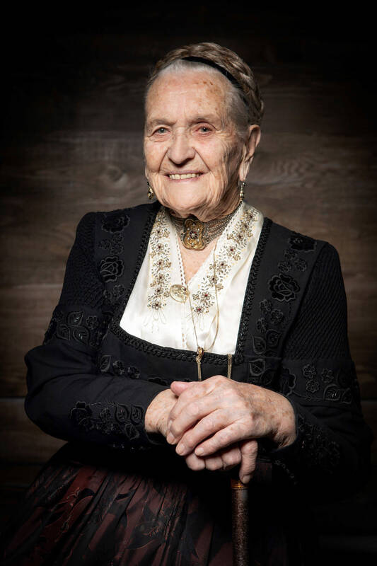 Portrait einer alten Frau in eleganter, reichbestickter Tracht mit edlem Schmuck.